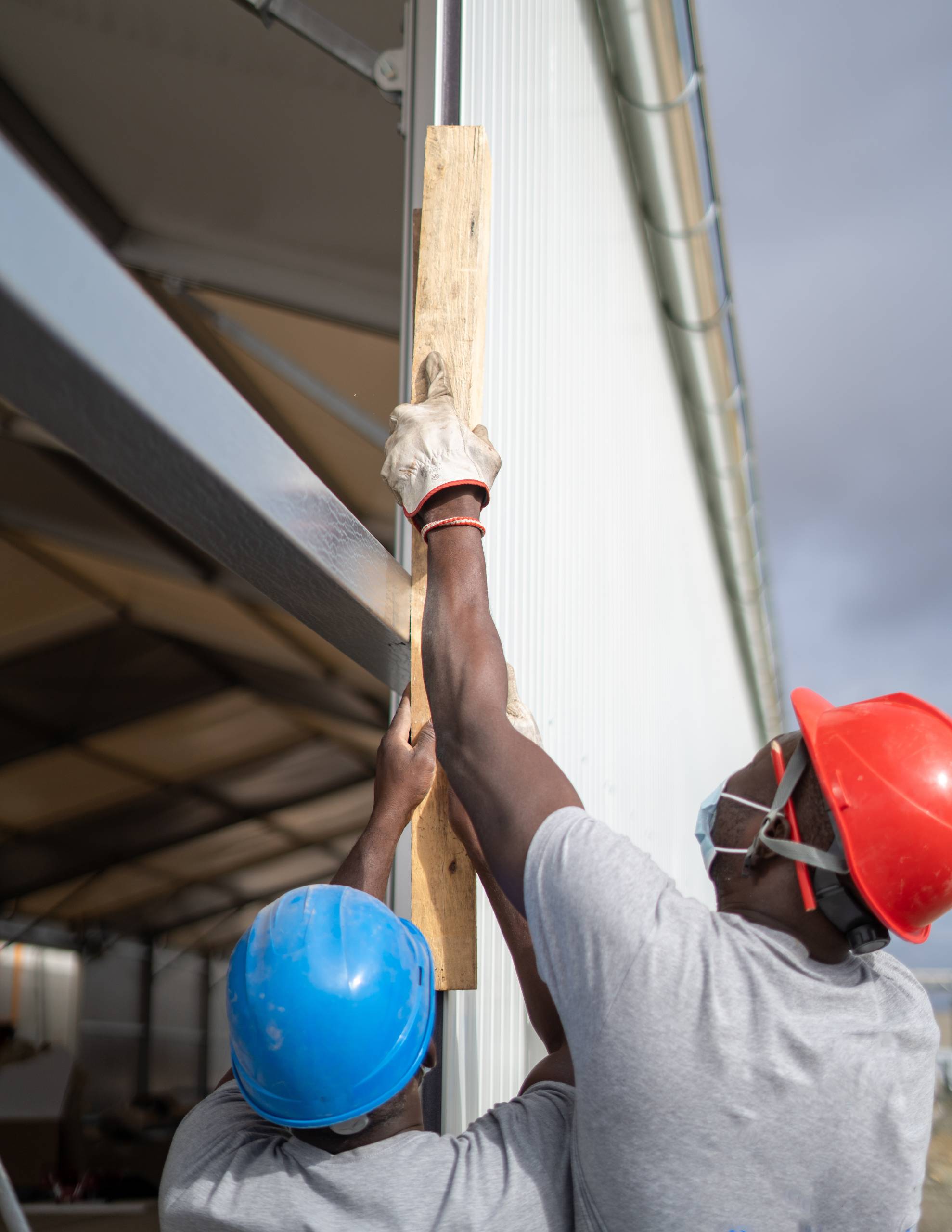 Two Afro-American builders wearing helmets and face masks while measuring the wall